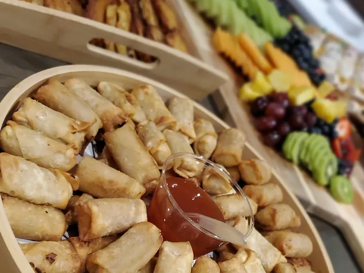 Crispy egg rolls with dipping sauce and a fresh fruit platter on a catering table